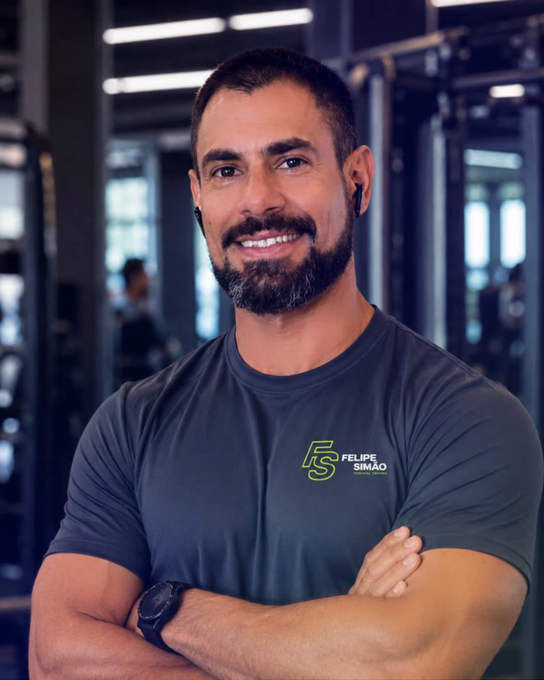 Felipe Simão, personal trainer, em pé de braços cruzados na academia
